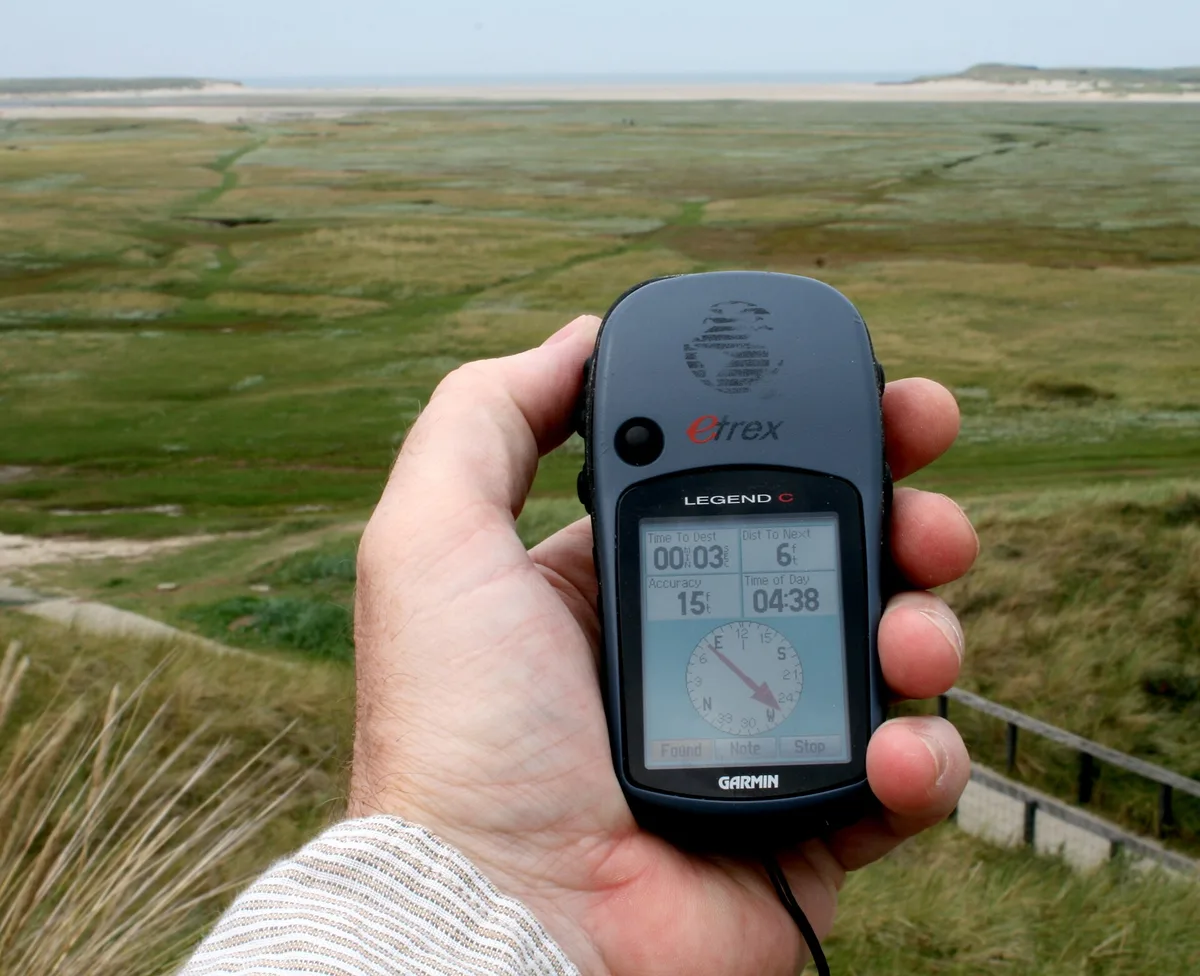 Walker holding a Garmin eTrex handheld GPS for hiking above green coastal grassland