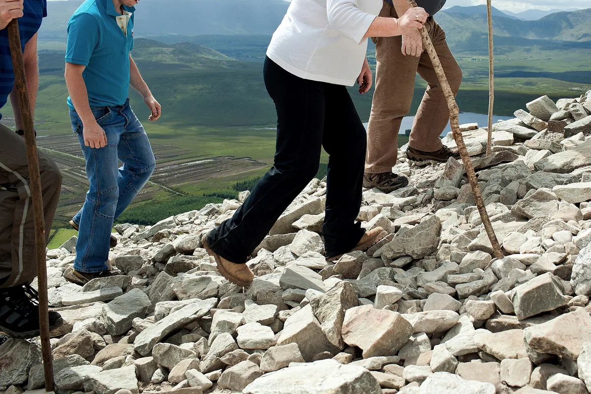 Pilgrims climbing the loose scree path on Croagh Patrick with the Mayo countryside far below