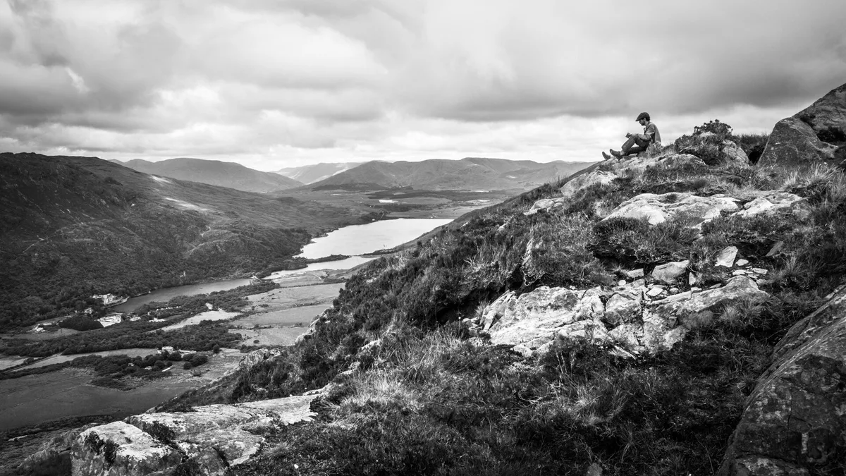 A lone walker reading in the Irish hills above a lough, the kind of quiet the best hiking books are written for