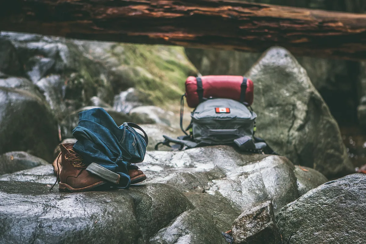 Backpacking checklist essentials: walking boots, clothes and a packed rucksack laid out on rocks